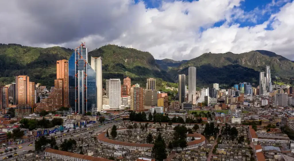 Vista panorámica de Bogotá con la Plaza de Toros de Santamaría, edificios modernos y el Cerro de Monserrate al fondo. Representación de la vida urbana en la capital de Colombia.